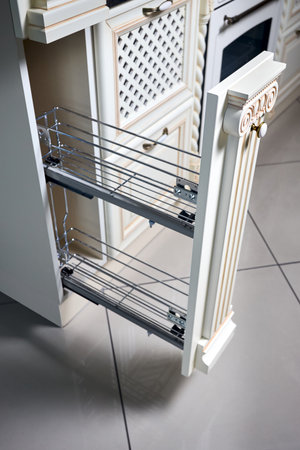 Pull out spice rack cabinet filler pantry. Interior of modern kitchen in classic style with golden elements in beige colors. Vertical drawer for spices shelf under countertop with front wooden panel.の写真素材