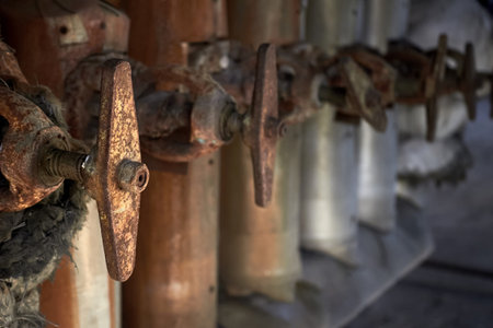 Brown industrial valves in a row on petrochemical plant pipelines system selective focus over out of...
