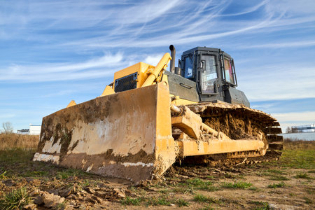Yellow dirty excavator in career moves overburden. Bulldozer crawler combs the ground, with blue sky in the background, wide angle bottom view with copy space.の写真素材