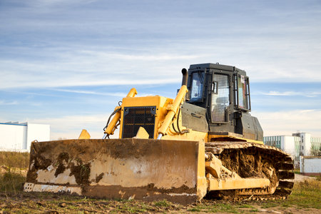 Yellow dirty excavator in career moves overburden. Bulldozer crawler combs the ground, with blue sky in the background, three quarter front view with copy space.の写真素材
