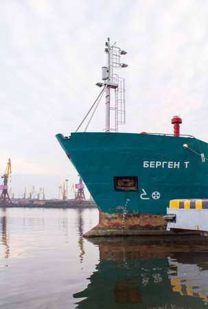 The bow of the ship at the shore on the embankment against the background of cranes vertical photo