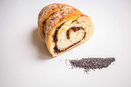 Sweet roll with poppy in cut on a white background next to a handful of poppyの写真素材