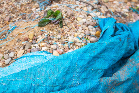 Blue tarp in the foreground sheltering a pile of sand and stones