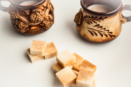 Reed sugar in the form of cubes lies against the backdrop of beautiful ceramic mugsの写真素材