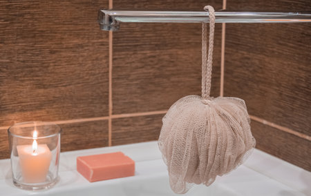 A washcloth hangs on a water tap close-up against a backdrop of pink soap and lit candlesの写真素材