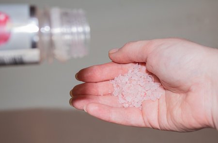 Pink sea salt is poured into the womans hand from the bottleの写真素材