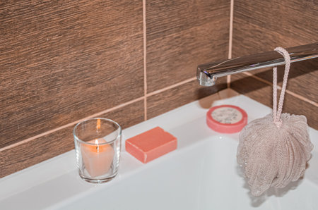 A washcloth hangs on a water tap against a backdrop of pink soap and lit candles