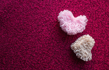 Two fluffy pompoms made of pink and beige heart-shaped ponies on a crimson backgroundの写真素材
