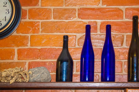 Glass colored bottles stand on a wooden shelf near round hoursの写真素材