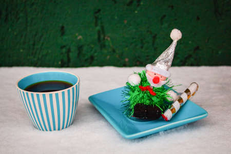 Christmas grandpas toy on a blue saucer next to a cup of black coffee in the snowの写真素材