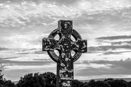 A cross is standing in a field with a cloudy sky in the background. The cross is old and has a weathered appearance. The sky is overcast, giving the scene a somber and melancholic moodの写真素材