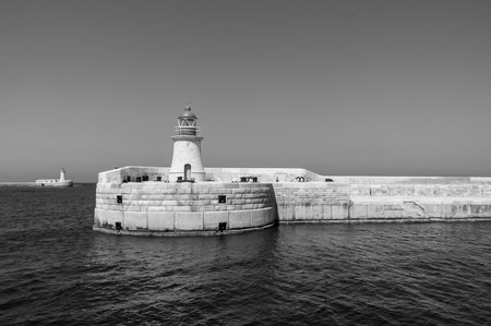 A lighthouse is on a rocky shoreline. The water is calm and the sky is clear. The lighthouse is the only structure visible in the sceneの写真素材