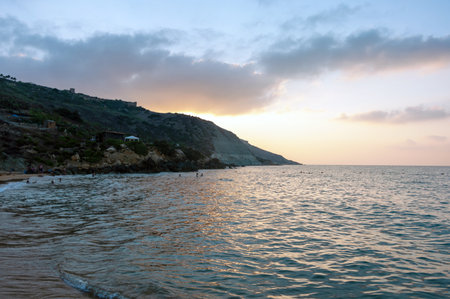 A beautiful sunset over the ocean with a beach in the background. The sky is filled with clouds, creating a serene and peaceful atmosphereの写真素材