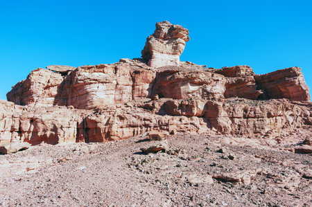 A large rock formation with a small hill in the background. The sky is clear and blue. Concept of solitude and isolationの写真素材