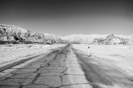 A desolate road with a few rocks and a sign. The road is empty and the sky is clearの写真素材