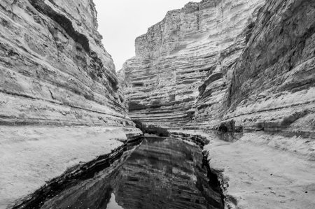 A black and white photo of a river with a rocky canyon in the background. The water is calm and the rocks are jaggedの写真素材