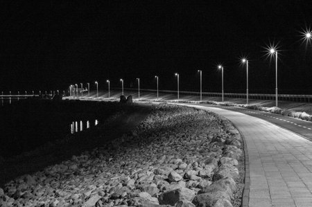 A dark night scene with a long road and a bridge. The road is lit up by street lights and the bridge is lit up by lightsの写真素材