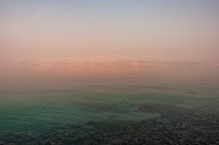 The sky is a beautiful shade of pink and the water is calm. The scene is serene and peacefulの写真素材