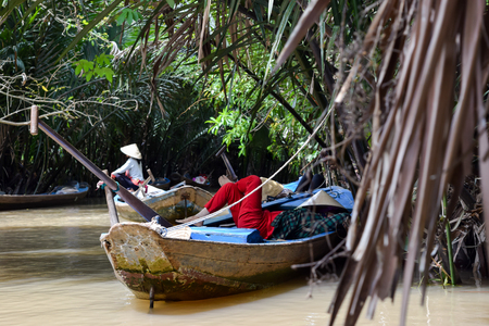 Oarsman resting in the boat in delta of Mekong river, Vietnam. Bright red trousers provide great contrast in the wilds of the green jungleの写真素材