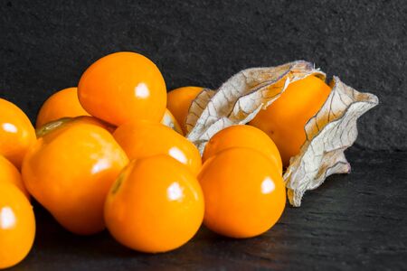 Cape Gooseberries on black rock surface background with the free pace. One of the Cape Gooseberries is with shellの写真素材