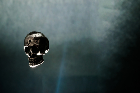 Metal skull levitating in air on black background illuminated by light. Mystical and spooky atmosphereの写真素材