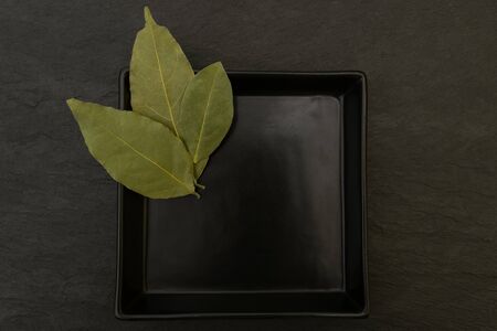 Three dried up bay leaves placed in black plate on black stone surface backgroundの写真素材