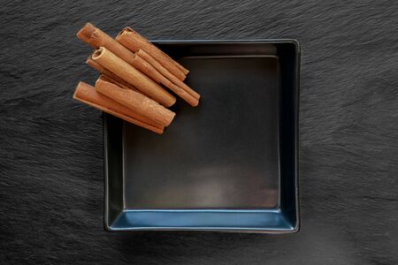 Pile dried cinnamon sticks placed on black plate which placed on black stone surface backgroundの写真素材