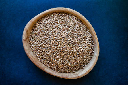 Buckwheat grains in wooden jar placed on deep blue background surfaceの写真素材