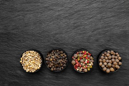 Black, green, pink, white and fragrant pepper grains in round jars placed on black stone surface backgroundの写真素材
