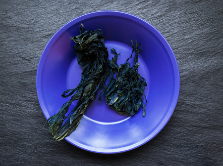 Dry bunch of seaweed in purple plate on black stone surface backgroundの写真素材
