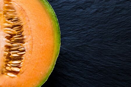 Half of Hami melon fruit on black stone background surface with free space. Background is blurry, the main focus on melonの写真素材