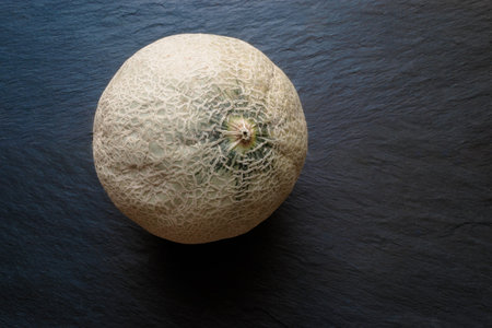 Full head of Hami melon fruit on black stone surface background with free space