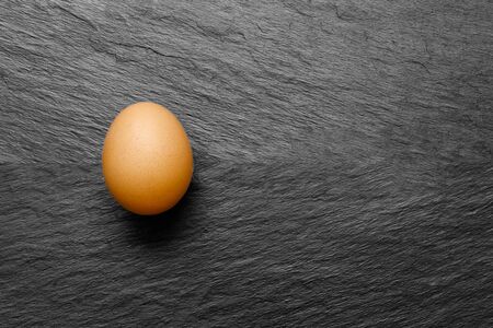 One chicken egg on black stone background surface with free spaceの写真素材