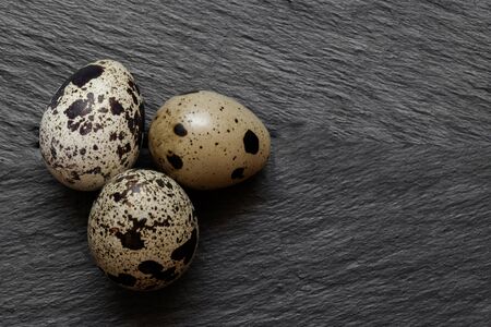 Three quail eggs on black stone blurry background surface with free spaceの写真素材