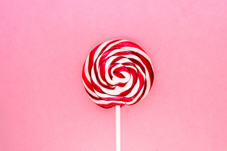 Round white and red lollipop with white stick on pink background surfaceの写真素材