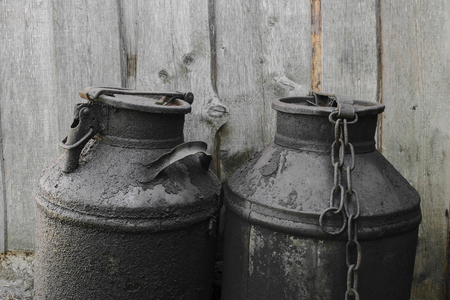 Black and oiled metal canisters in the countryside. Wooden wall in backgroundの写真素材