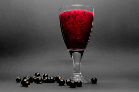 Glass of black currant red color cocktail in grey background with berries on itの写真素材