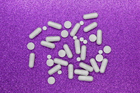 Bunch of different forms white medication pills on shining purple background surface