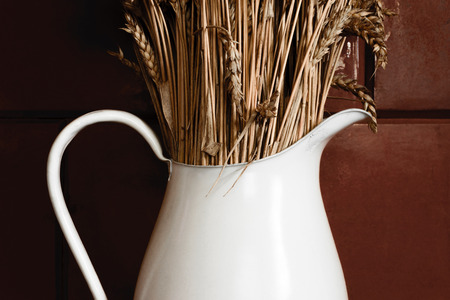 Old and white rustic pitcher with dry rye in front of brown wallの写真素材