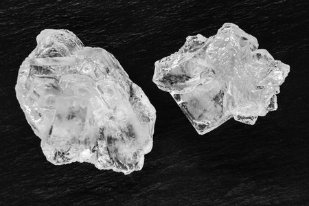 Top view of two sugar or salt crystals placed on black stone background surface