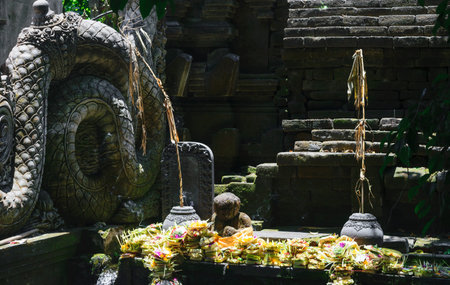 Traditional Bali temple with black stone sculptures and offerings for god made from banana leaves