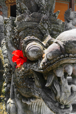 Very old dragon head shape stone sculpture covered with moss and lichens in Bali and decorated with red flower blossomの写真素材