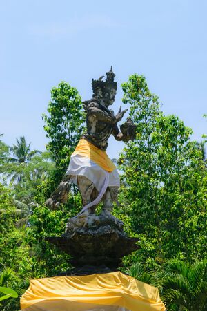 Bali, Indonesia. 6 OCT 2018. Traditional Bali god sculpture covered with skirt in front of blue sky and green treesのeditorial素材