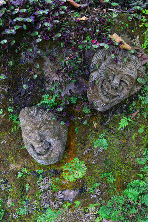 Traditional Bali smiling stone sculpture wall decorations covered with moss, lichens and vegetationの写真素材