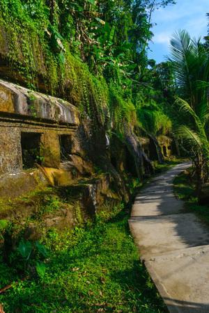 Carved in the stone ancient Gunung Kawi Temple with royal tombs illuminated by evening sun and leading path through the jungles in Bali, Indonesiaの写真素材