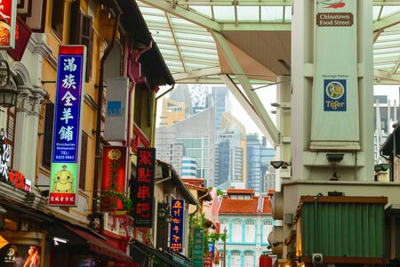 Singapore - 14 OCT 2018. Chinatown district with a lot of colorful cafeterias and restaurants signboards. Area covered with glass roof to protect from the rain. Skyscrapers in backgroundのeditorial素材