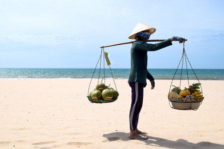 VIETNAM, Mui Ne - 27 MAR 2017. Beach fruit salesman walking on the beach in Vietnam. He is selling coconuts, bananas and other exotic fruitsのeditorial素材