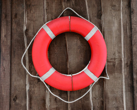 Red and round lifebuoy hanging on brown wooden wall. Part of lifebuoy covered with snowの写真素材
