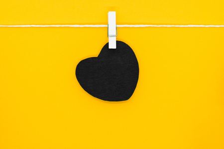 Black paper heart with copy space hanging on white rope and attached with white laundry pins on yellow backgroundの写真素材