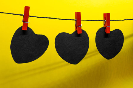Black paper hearts with copy space hanging on black rope and attached with red laundry pins on...